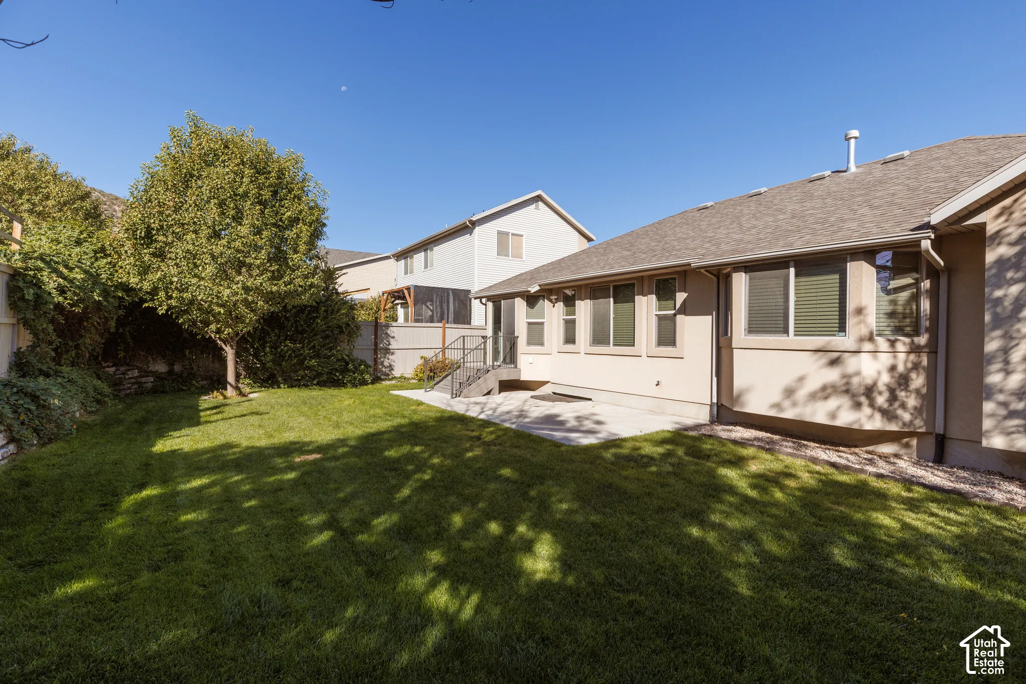 Expansive lawn area with mature trees, a concrete patio, and a stucco exterior with multiple windows