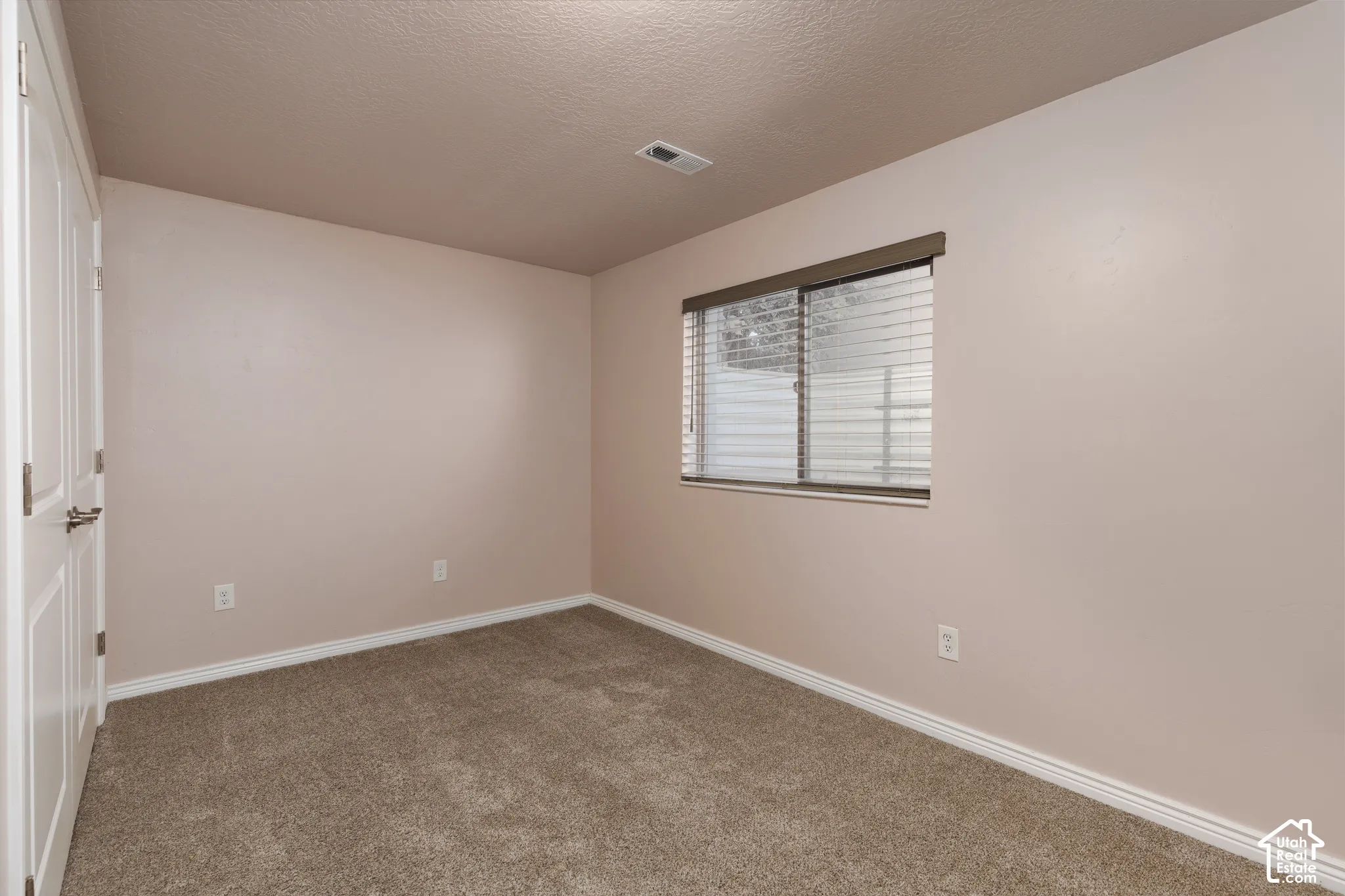 Neutral tone wall paint, textured ceiling, and window with blinds