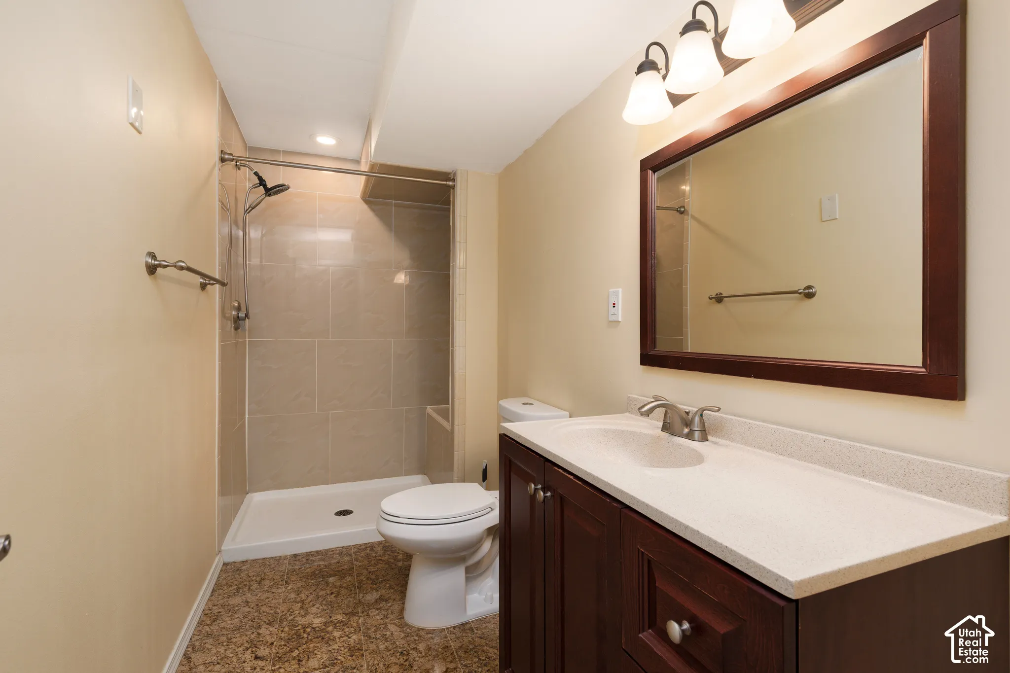 Dark wood-finish vanity with a light-colored countertop and integrated sink, brushed nickel faucet, large mirror, and three-bulb vanity light fixture