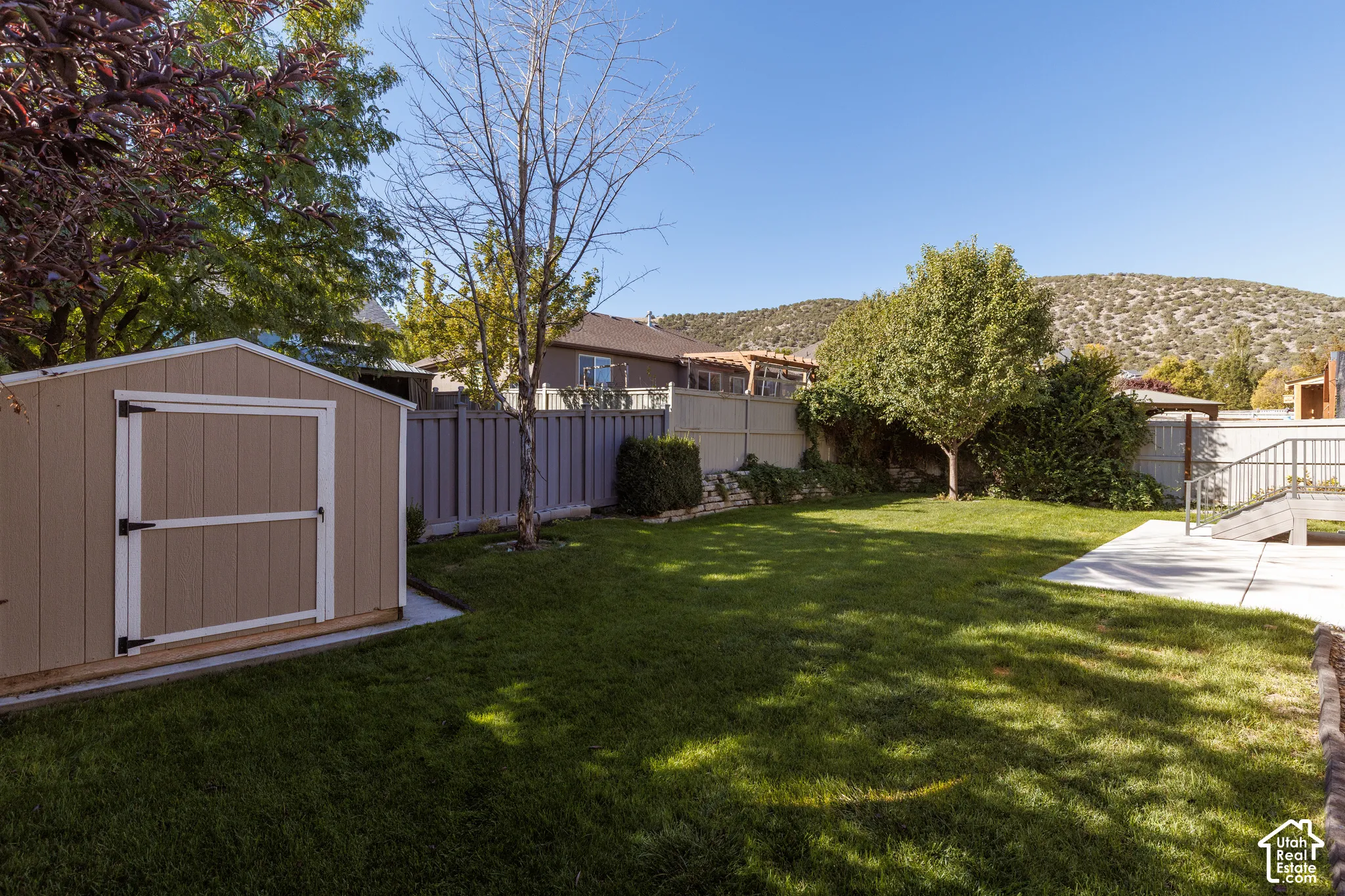 Expansive green lawn with a storage shed, concrete patio area, and perimeter fencing