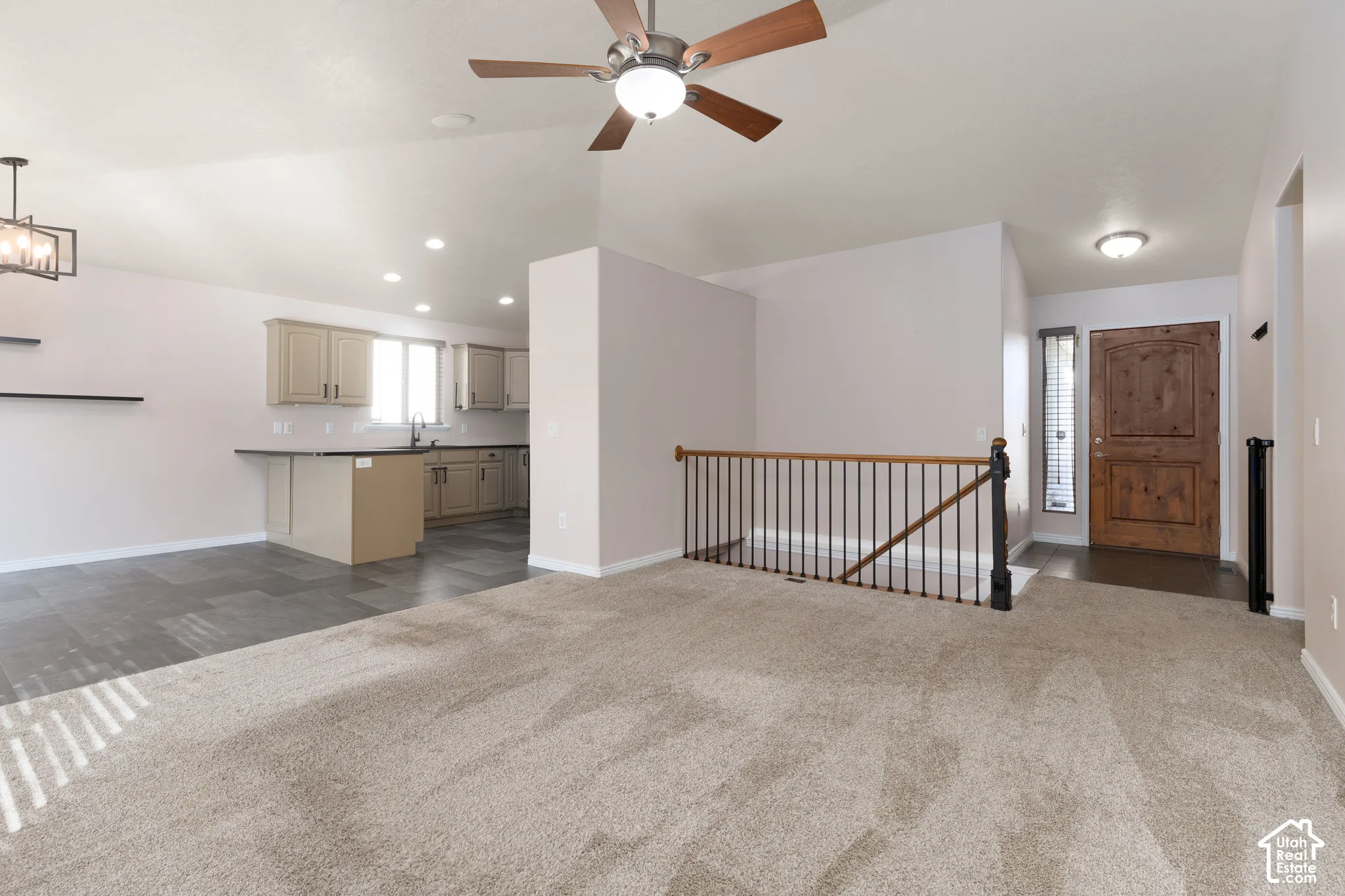 Vaulted ceiling with ceiling fan, wood-finish front door, metal spindle railing, kitchen with built-in cabinetry, and tile flooring
