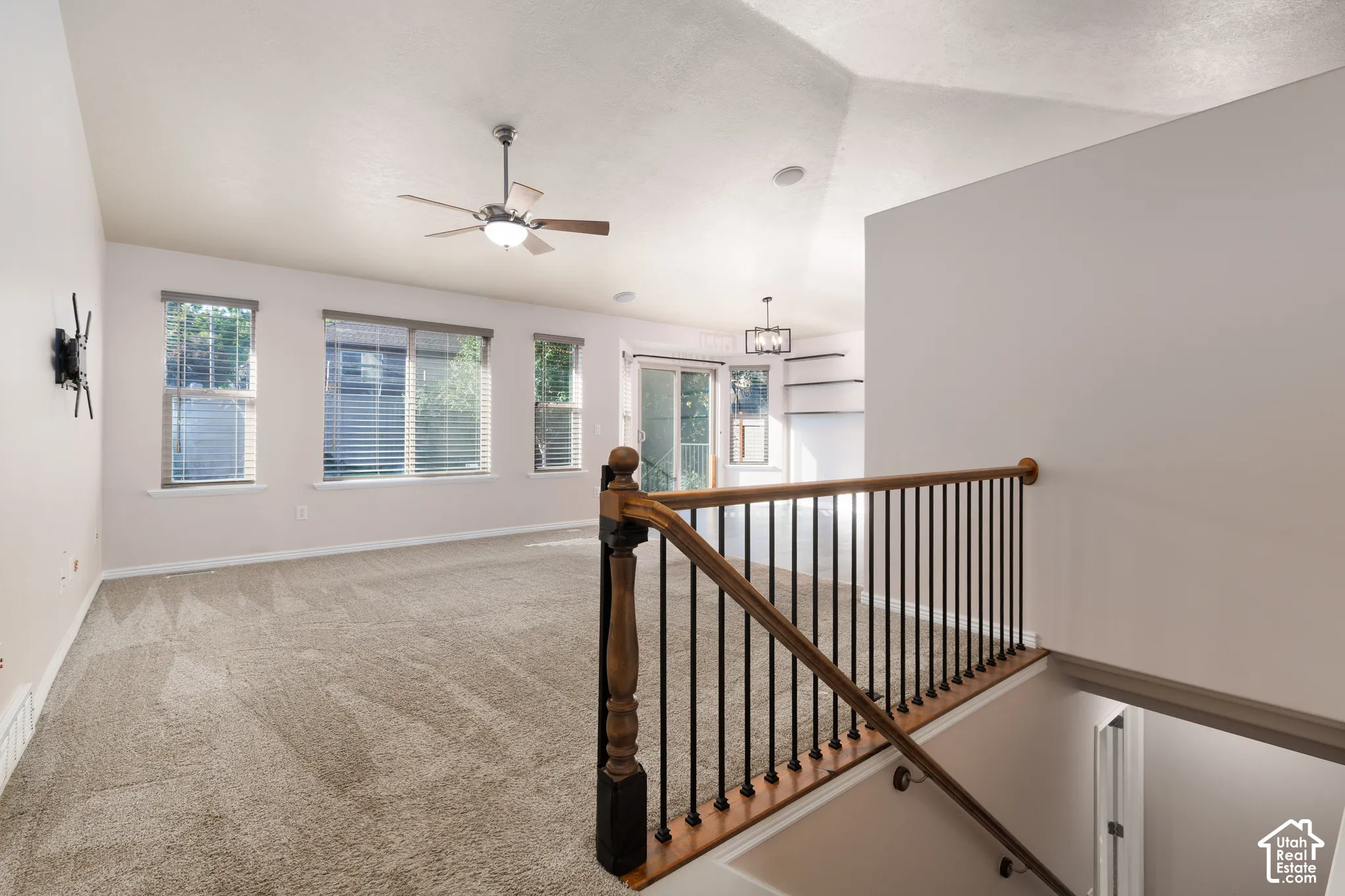 Carpeted living area with multiple windows, a ceiling fan, and staircase with wood railing and metal spindles