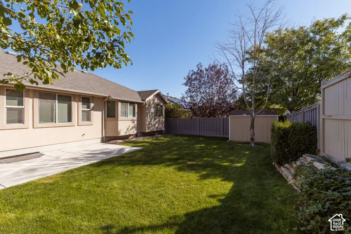 Expansive grassy yard featuring a concrete patio, exterior access, and a storage shed