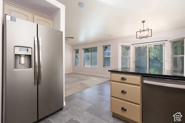 Stainless steel refrigerator with a side-by-side design, an in-door dispenser, light-toned cabinetry, and black countertops