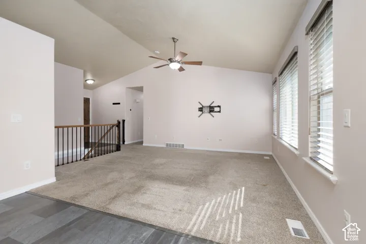 Vaulted ceiling with a ceiling fan, multiple windows with blinds, carpeted flooring, and a wood-finish flooring transition