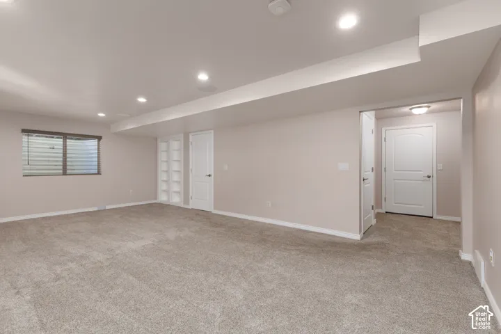 Spacious room featuring neutral carpeting, recessed lighting, a built-in shelving unit, and a window with blinds