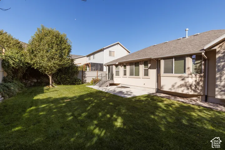 Expansive lawn area with mature trees, a concrete patio, and a stucco exterior with multiple windows