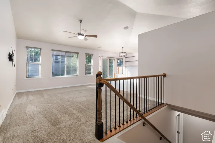 Carpeted living area with multiple windows, a ceiling fan, and staircase with wood railing and metal spindles