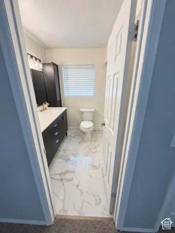 White paneled door opening to a bathroom featuring a dark wood-finish vanity with a white countertop, gold-tone faucet, and an illuminated mirror