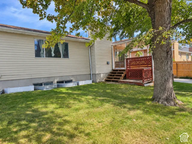 Rear exterior featuring light-colored siding, a covered deck with lattice railing, and a manicured lawn