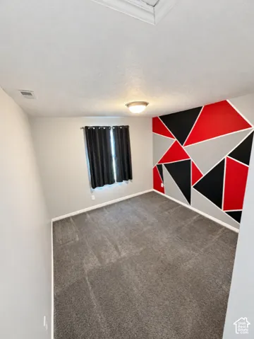 Wall-to-wall carpeting, window with dark drapes, ceiling-mounted light fixture, and geometric accent wall