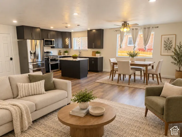 Open-concept living space with wood-finish flooring, a kitchen island, stainless steel appliances, dark cabinetry, and recessed lighting