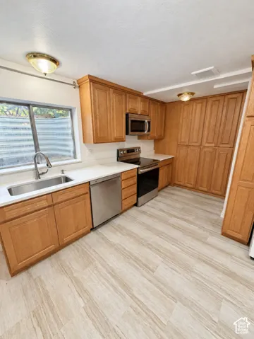 Wood-finish flooring, stainless steel appliances, light wood cabinetry, white countertops, and a stainless steel sink