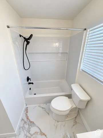 Full bathroom featuring a white subway tile shower surround with a built-in niche, white bathtub, black shower fixtures, and marble-look floor tiles