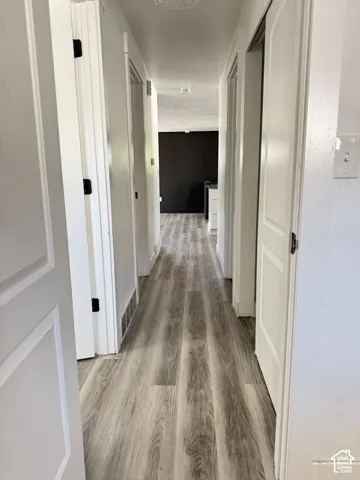 Hallway with wood-finish flooring, white walls, and white doors with black hardware