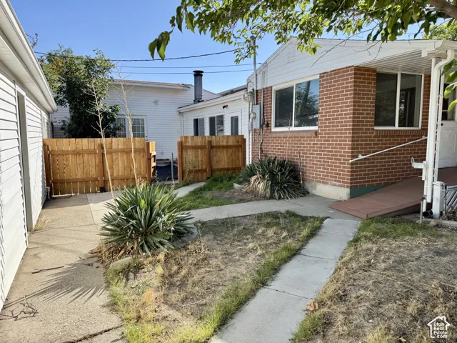 Brick exterior with multiple windows, concrete pathways, wooden fencing, and established plantings
