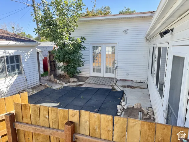 White siding exterior featuring double French doors, wood-finish decking, and a wood privacy fence