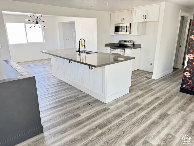 Open-concept kitchen with a central island, stainless steel microwave, white cabinetry, and wood-finish flooring
