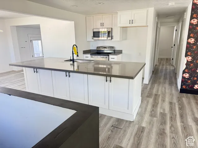Kitchen featuring a large island with a dark countertop, white shaker-style cabinetry, and stainless-steel appliances