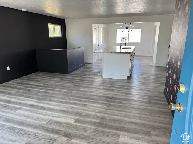 Spacious living area featuring wood-finish flooring, a contemporary kitchen island with a sink, and a modern chandelier