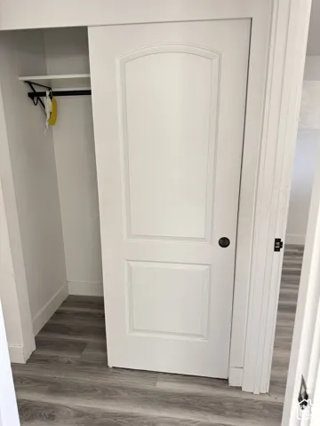 Closet with wood-finish flooring, a white shelf, and a black hanging rod