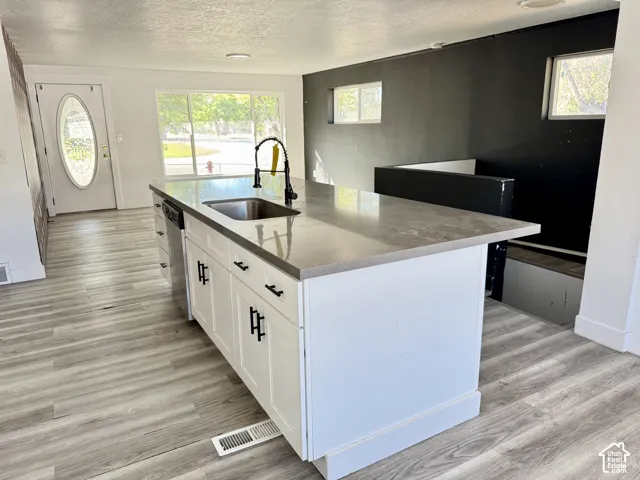 Central kitchen island with white cabinetry and a light-toned countertop, integrated stainless steel sink with a matte black faucet, and wood-finish flooring throughout