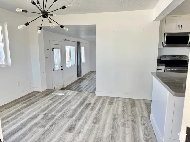 Wood-finish flooring throughout, modern sputnik chandelier, white cabinetry, stainless steel appliances, and a kitchen peninsula with a stone countertop