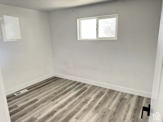 Wood-finish flooring with white trim, white walls, and a white-framed window