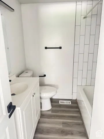 White vanity with integrated sink, wood-finish flooring, white subway tile shower surround, and matte black hardware