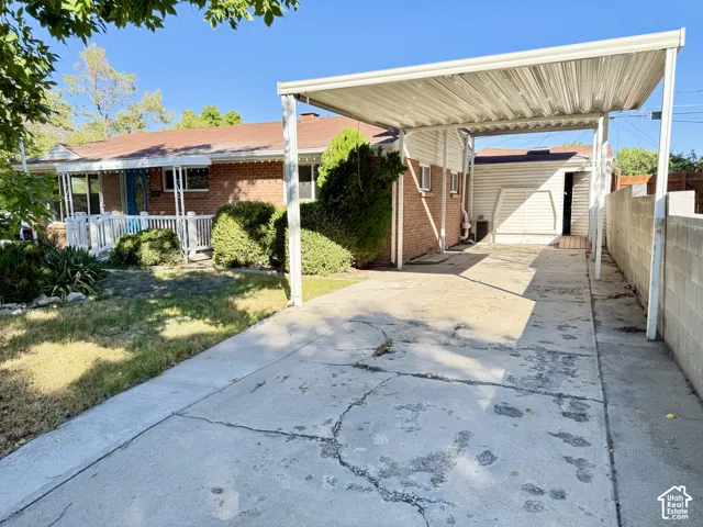 Red brick exterior with a front porch featuring white railing, mature landscaping, and an attached carport