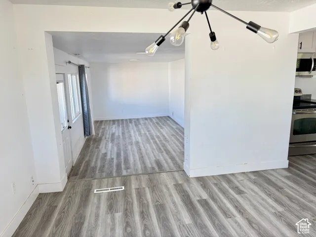 Open concept floor plan featuring wood-finish flooring, white walls, and a modern black chandelier