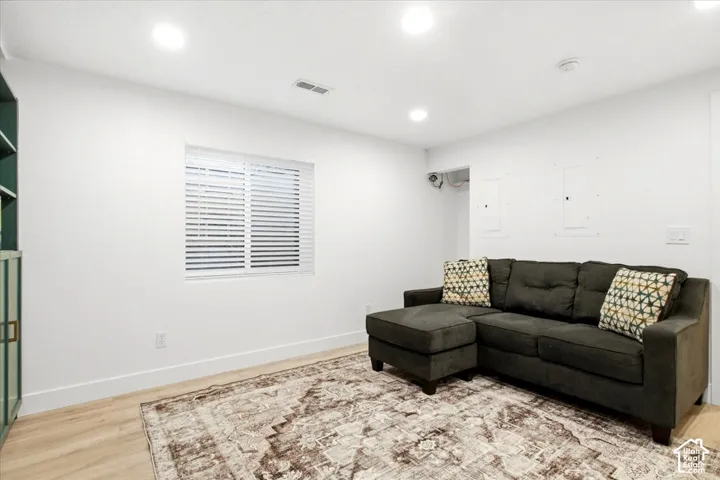 Recessed lighting illuminates the space, featuring a window with white blinds and wood-finish flooring