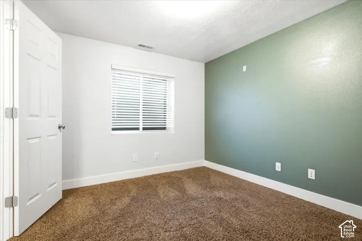 Carpeted room featuring a window with horizontal blinds, white door, and contrasting accent wall