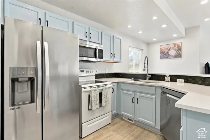 Kitchen featuring light blue cabinetry, stainless steel appliances, light-toned countertops, a dark tile backsplash, and recessed lighting