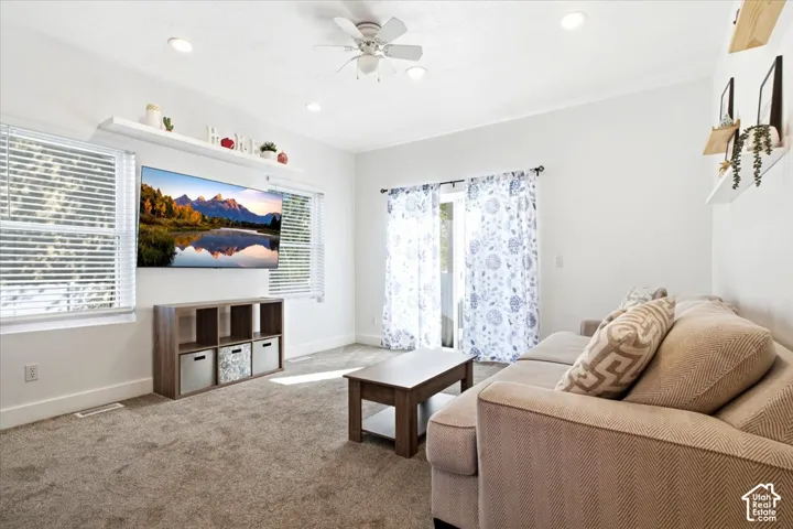 Carpeted living area featuring a ceiling fan, recessed lighting, and a glass-paned door