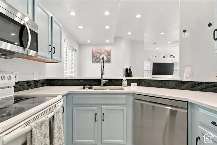 Kitchen featuring light blue cabinetry with black hardware, white countertops, a dark mosaic tile backsplash, and stainless steel appliances