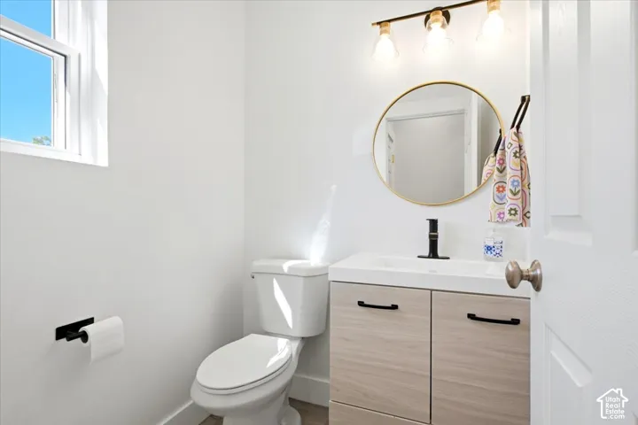 Powder room featuring a single-pane window, round gold-finish mirror, vanity with wood-finish cabinetry, and a black-finish faucet