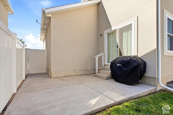 Concrete patio with sliding glass door access, white vinyl fencing, and a side gate