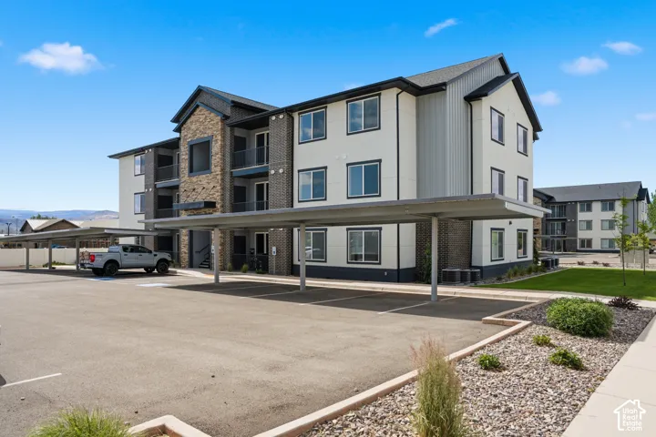Contemporary apartment building featuring stone and panel siding, covered parking, and multiple balconies