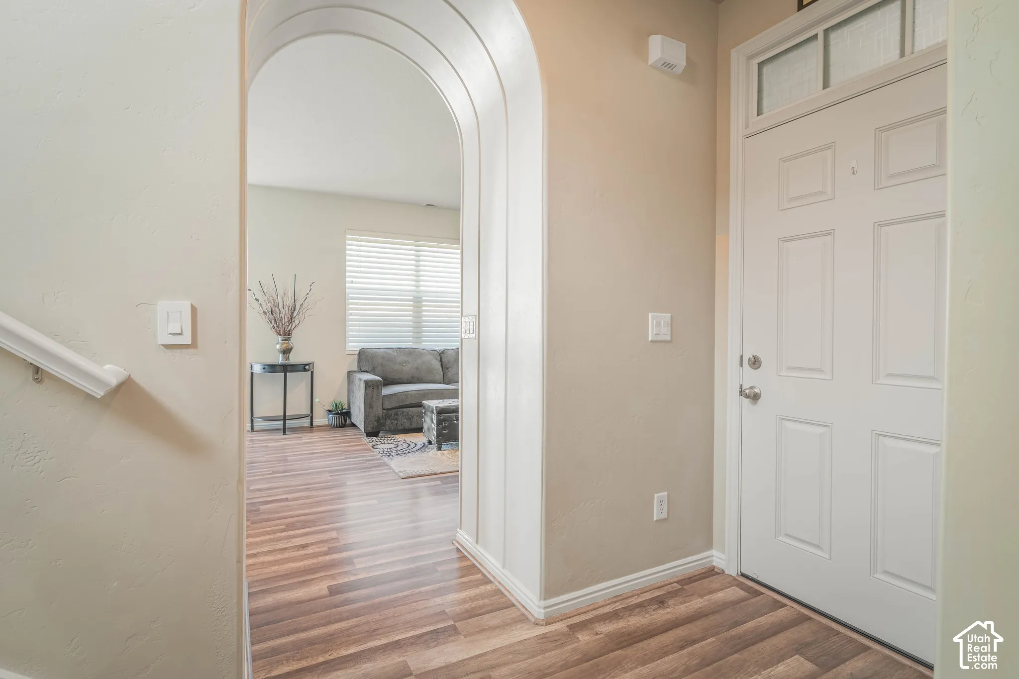 Entryway featuring a paneled door with transom window, an arched doorway, wood-finish flooring, and a white handrail