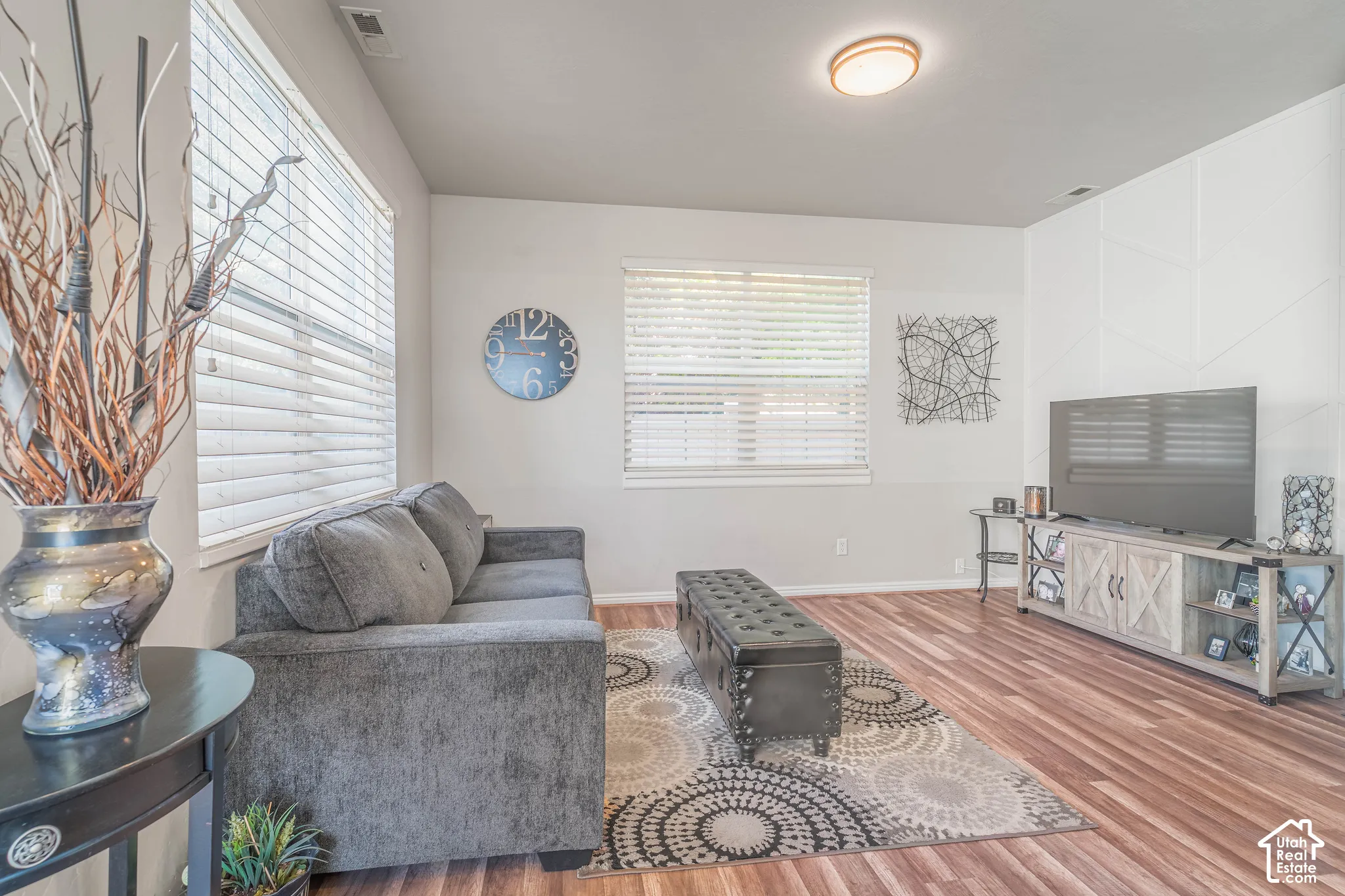 Wood-finish flooring throughout, multiple windows with blinds, recessed ceiling lighting, and a paneled accent wall