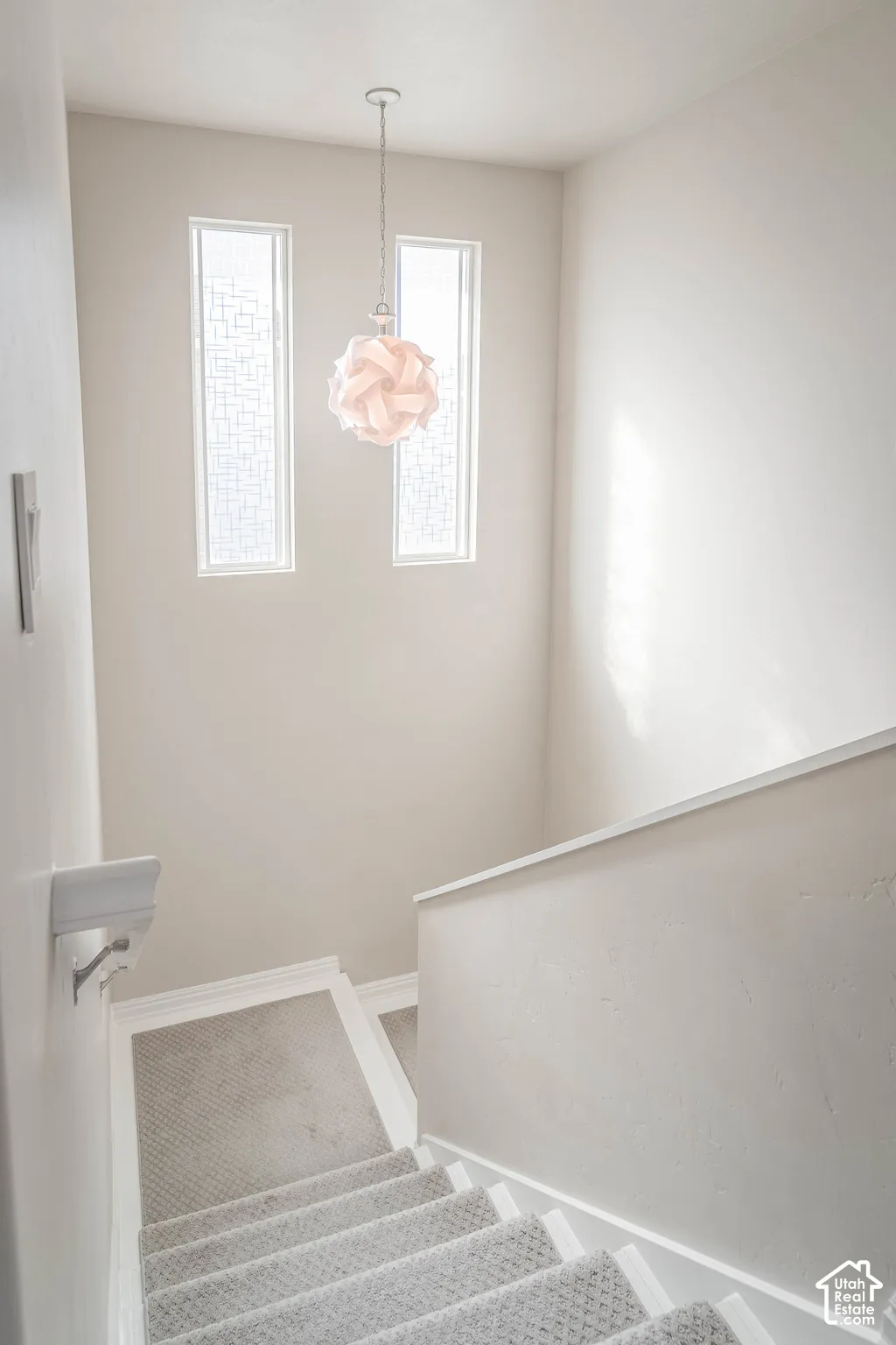 Staircase featuring carpeted treads, white risers, and a contemporary pendant light fixture