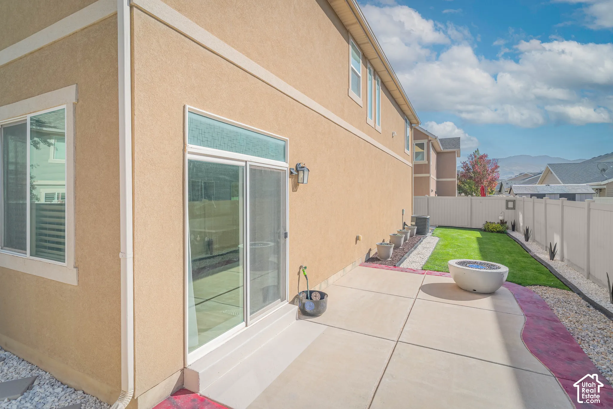 Stucco exterior with multiple windows, sliding glass door, concrete patio, and a manicured lawn