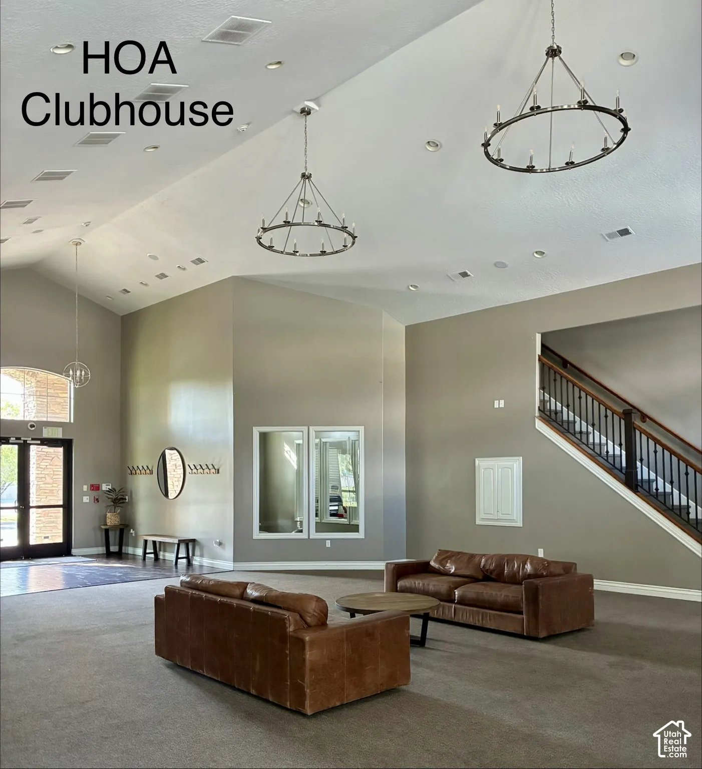 Vaulted ceilings with recessed lighting, two wrought iron chandeliers, a large entry door with arched transom, a wood and wrought iron staircase, and framed wall mirrors