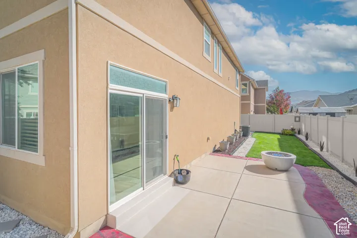 Stucco exterior with multiple windows, sliding glass door, concrete patio, and a manicured lawn