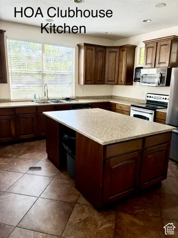 Kitchen featuring dark wood cabinetry, light-toned countertops, a central island, stainless steel appliances, and tile flooring