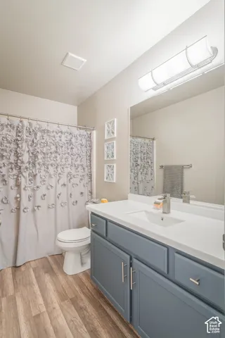 Wood-finish flooring, single vanity with a white countertop, recessed lighting, and a wall-mounted light fixture