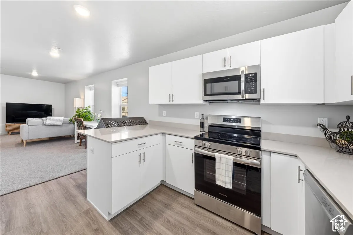 Kitchen featuring white cabinetry, light-toned countertops, wood-finish flooring, and stainless steel appliances including a range and microwave