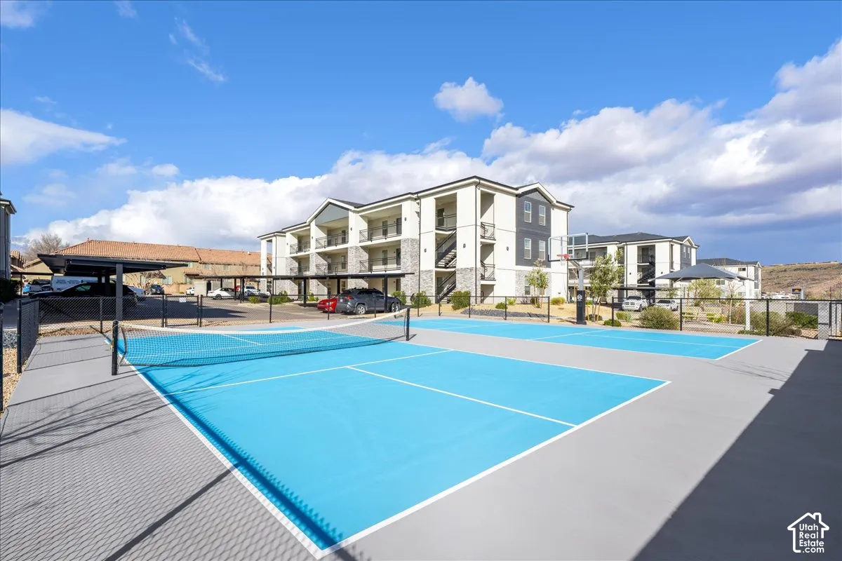 Recreational courts with blue surfacing, surrounded by a black metal fence, and an adjacent basketball hoop