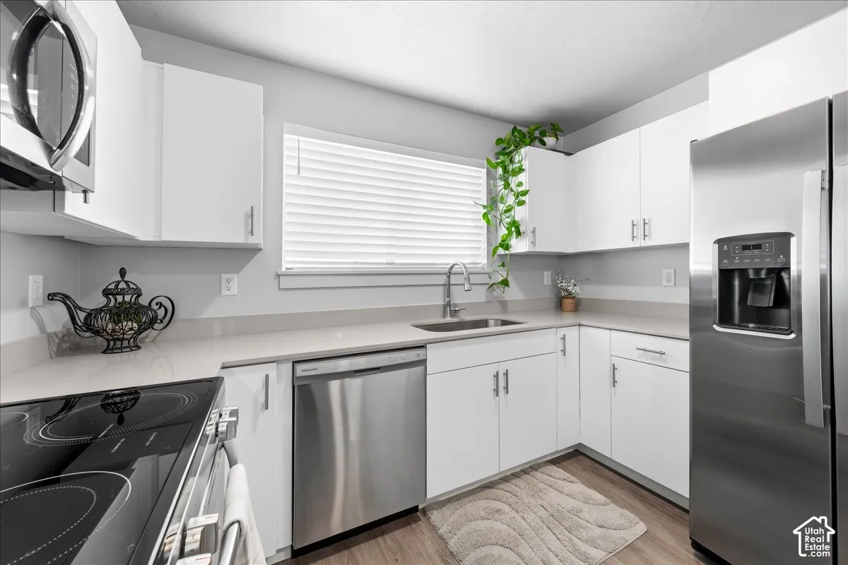 Kitchen featuring white cabinetry, light countertops, stainless steel appliances, and wood-finish flooring
